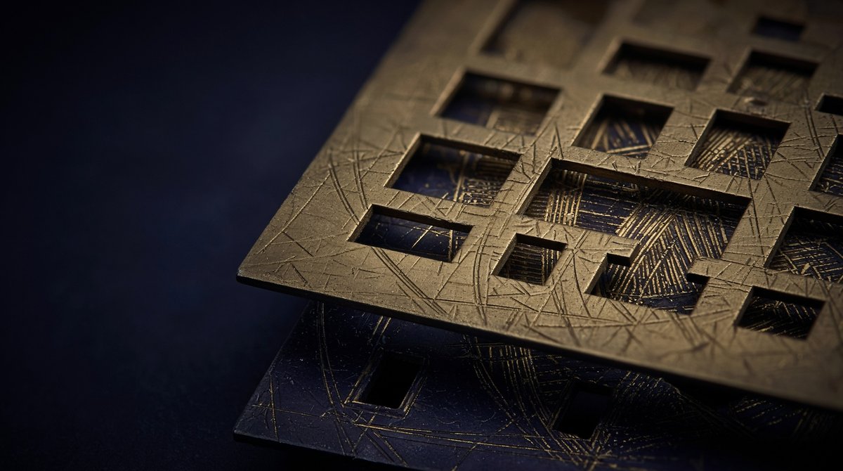 A pierced brass plate held just above a dark engraved one, the engraving showing through its windows