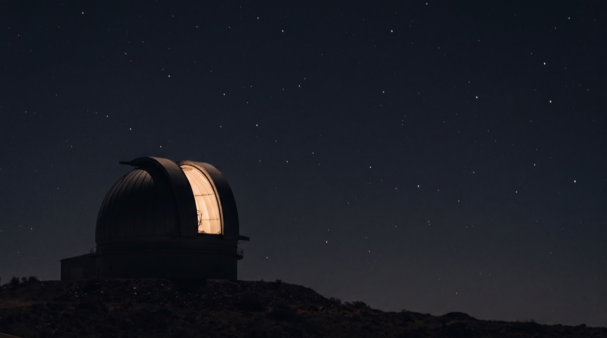 An observatory dome at night, its open slit glowing warmly from within