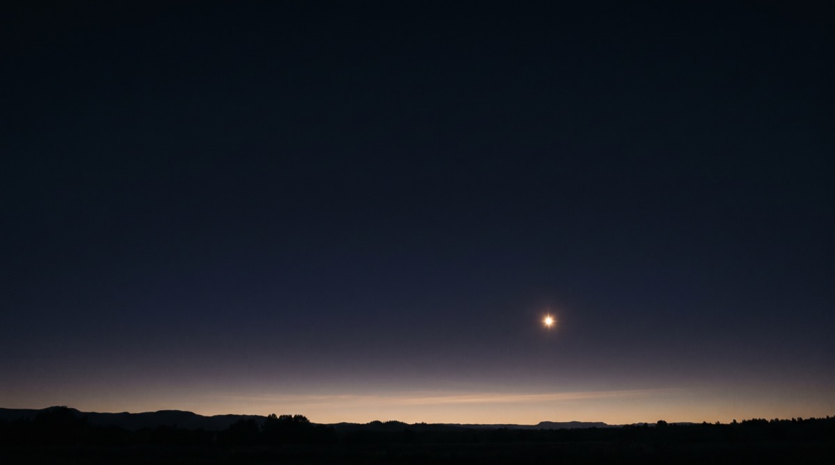 A single bright star low over a dark horizon at dusk